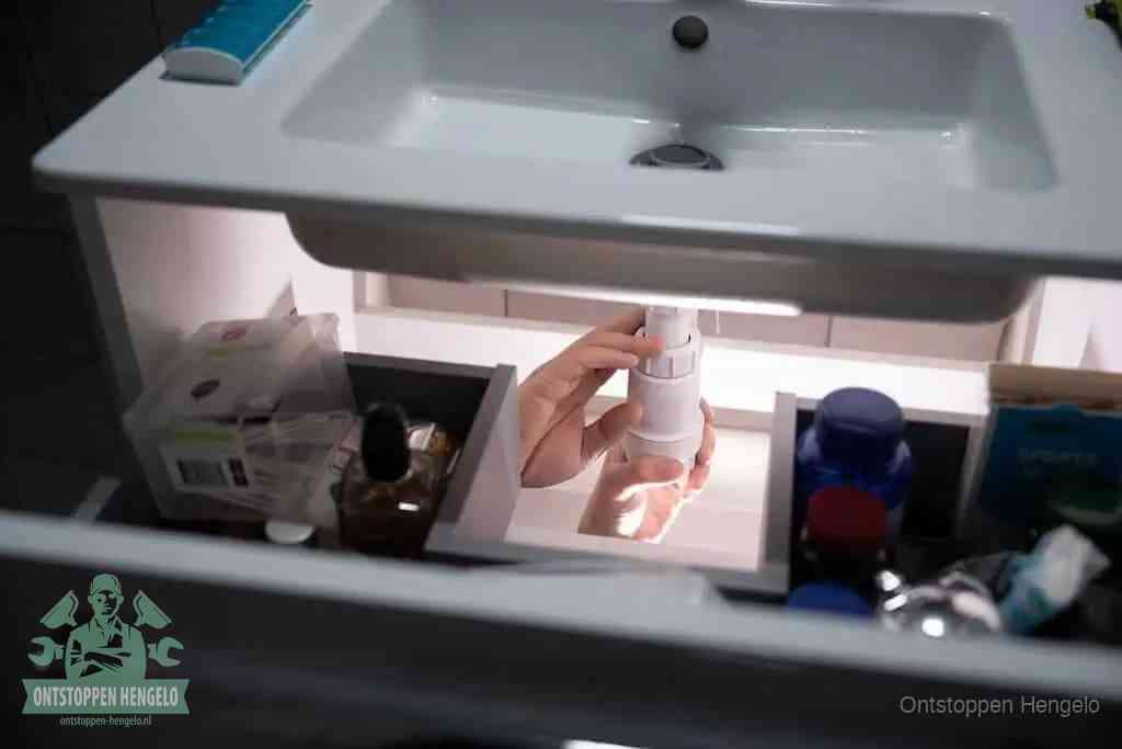 Een pompfles met zeep boven een wastafel, de heet water en afwasmiddel-methode om een vetprop in de afvoer los te maken in Hengelo