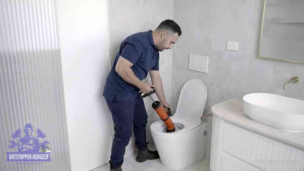Een monteur buigt over een wandcloset en duwt met de hand een persluchtontstopper in de toiletpot om de verstopping handmatig los te maken in Hengelo