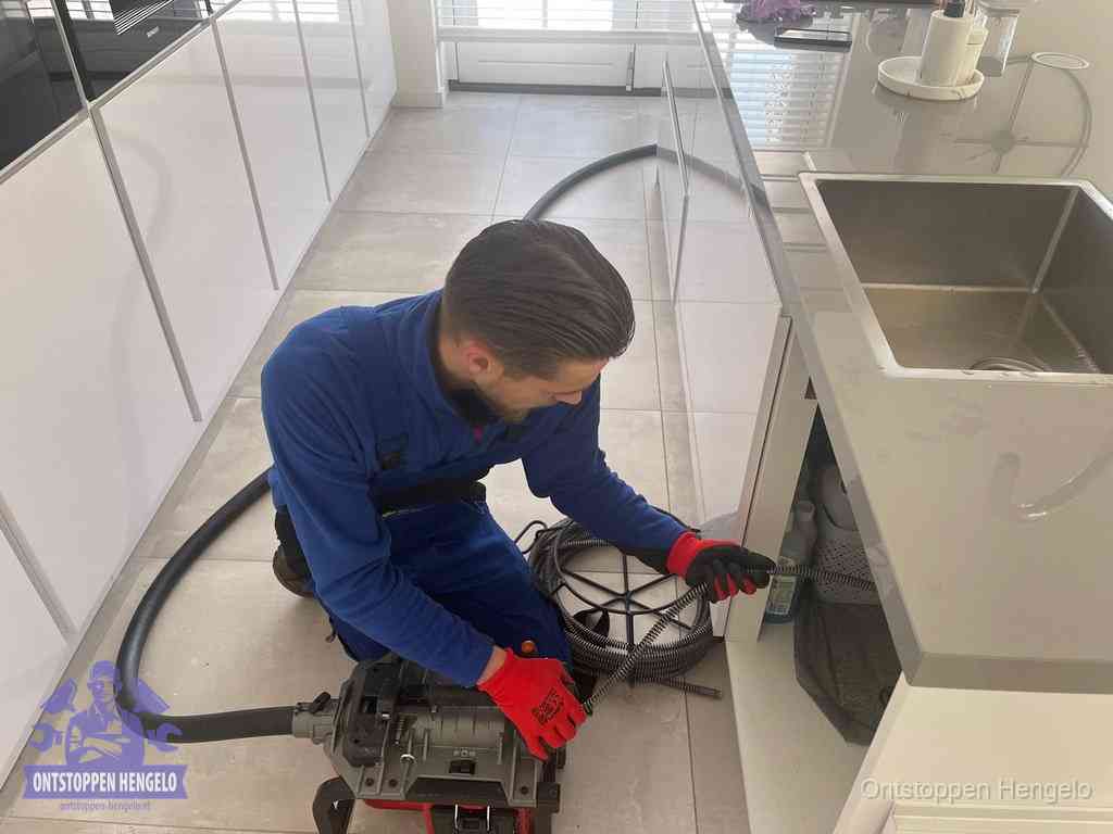 Een monteur ontstopt de keukenafvoer onder de spoelbak met een elektrische veermachine in Hengelo