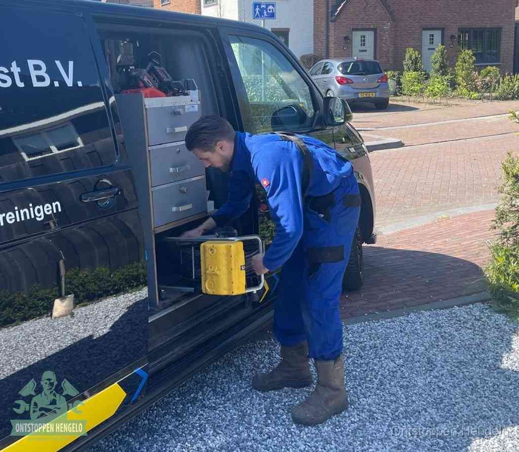 Een monteur pakt buiten op de oprit gereedschap uit de bedrijfsbus, het moment om een professional in te schakelen voor een verstopte afvoer in Hengelo