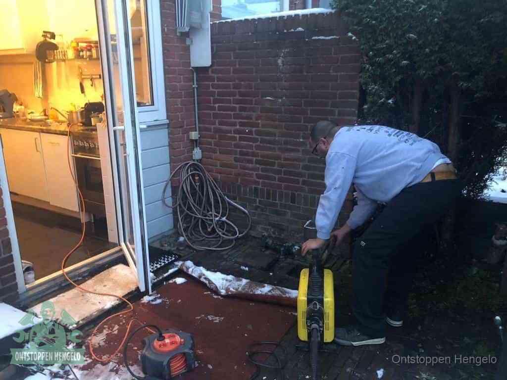 Een monteur werkt buiten bij een open riool-/grondput met een elektrische ontstoppingsmachine om een verborgen afvoerprobleem op te sporen in Hengelo