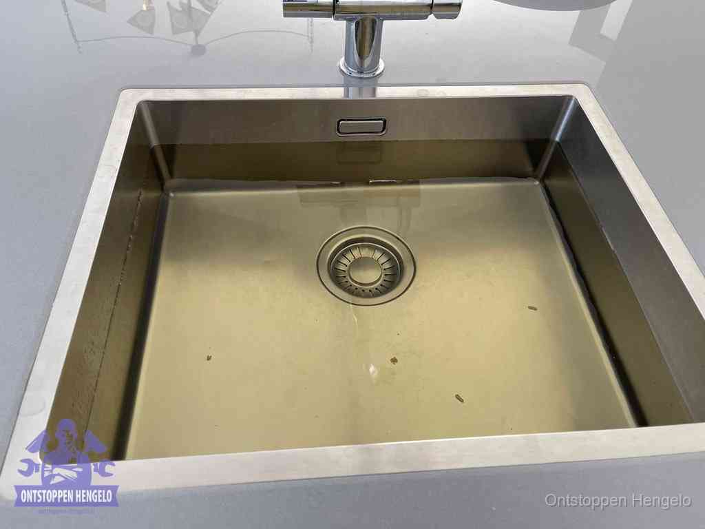 Stilstaand water in een rvs spoelbak dat niet wegloopt, een duidelijk signaal van een gootsteenverstopping in Hengelo