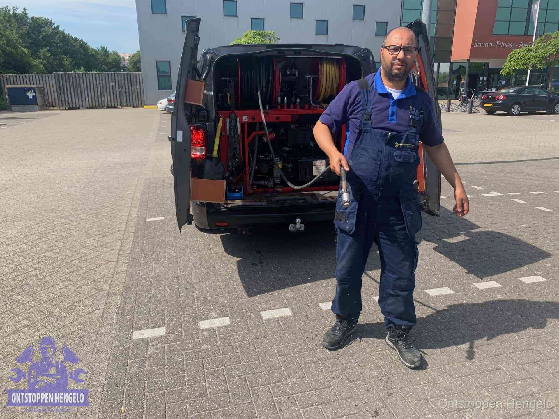 Een monteur bij zijn bestelbus met een hogedruk- en rioolreinigingsunit, klaar om de oorzaak van terugkerende wc-verstoppingen aan te pakken in Hengelo