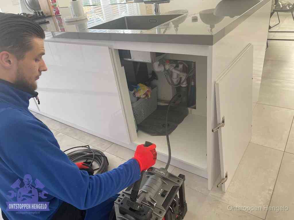 Monteur ontstopt met een veermachine een verstopte afvoer onder de gootsteen in Hengelo