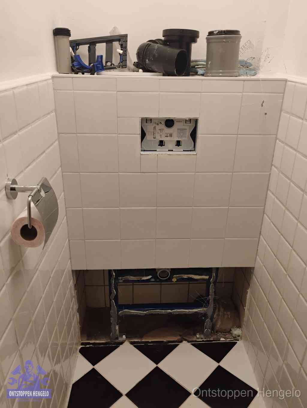 Een toiletruimte waar het hangtoilet en de inbouwreservoir-onderdelen zijn vrijgelegd voor onderhoud, periodiek nazicht voorkomt een wc-verstopping in Hengelo