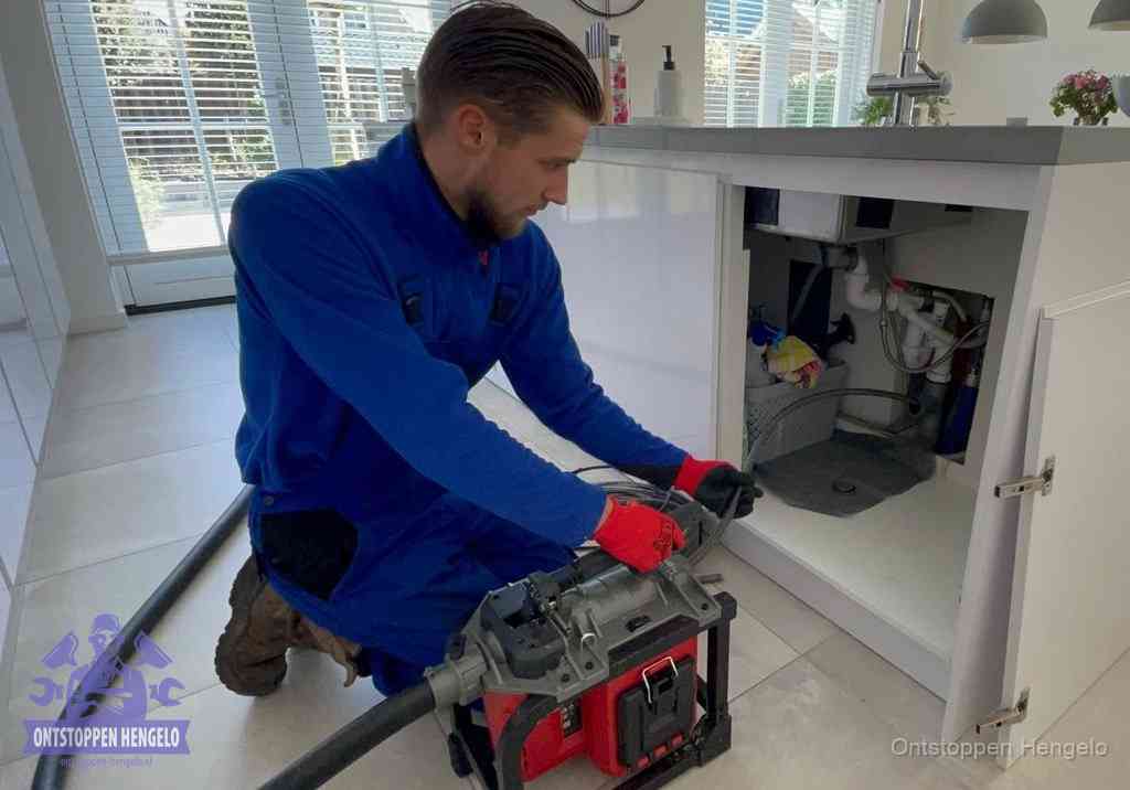 Een monteur voert een professionele elektrische ontstoppingsmachine in de afvoer onder de spoelbak tijdens het gootsteen ontstoppen in Hengelo