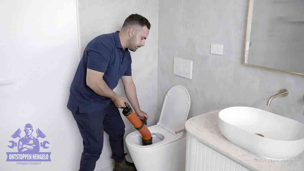 Een man gebruikt een handmatige luchtdruk-ontstopper in een modern betegeld toilet om zelf de wc te ontstoppen in Hengelo